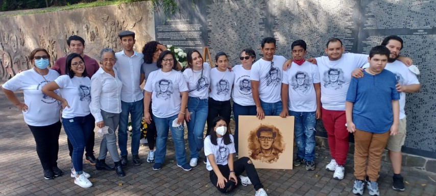 Dieciséis personas, todos familiares y descendientes de Efraín, posan frente a un muro conmemorativo con camisetas blancas con una ilustración del rostro de Efraín.