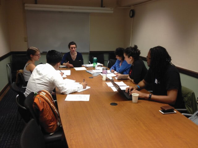 Seis personas alrededor de una mesa de conferencias en el campus de la Universidad de Washington, tomando notas y participando en una discusión.